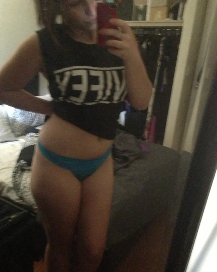 Jeune femme brune en débardeur noir et culotte turquoise, selfie miroir dans une chambre