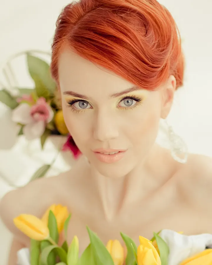 Jeune femme rousse aux yeux bleus, maquillage jaune vif, fleurs en premier plan