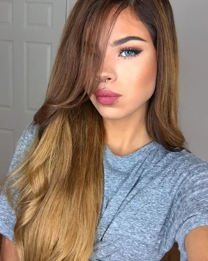 Femme aux cheveux longs, portant un haut gris et un short rose, prenant un selfie devant un miroir, dans une chambre.
