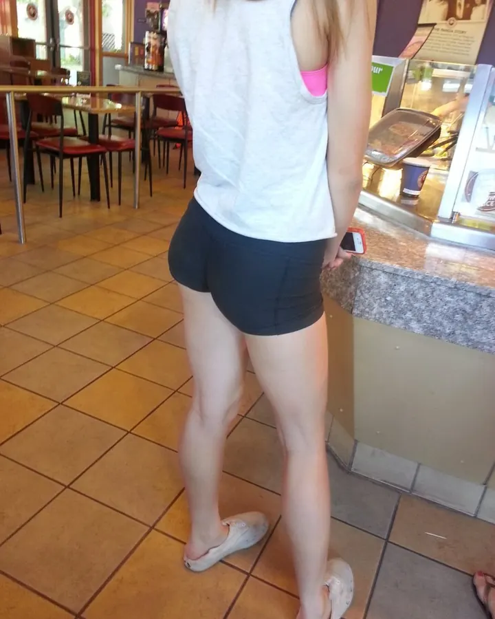 Femme asiatique aux cheveux blonds posant en lingerie noire, les mains sur les hanches, dans une pièce avec papier peint floral