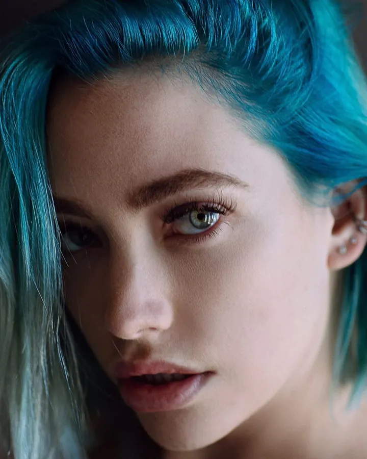 Femme en haut bleu, regardant vers la caméra, cheveux bleus, oreilles percées.