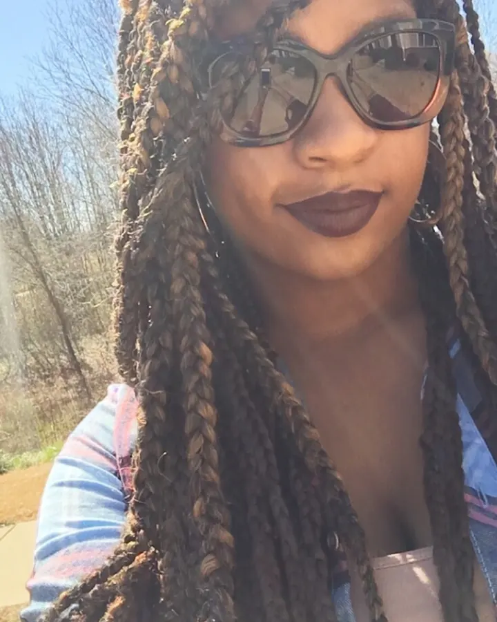 Femme africaine avec tresses et lunettes de soleil, souriante en extérieur
