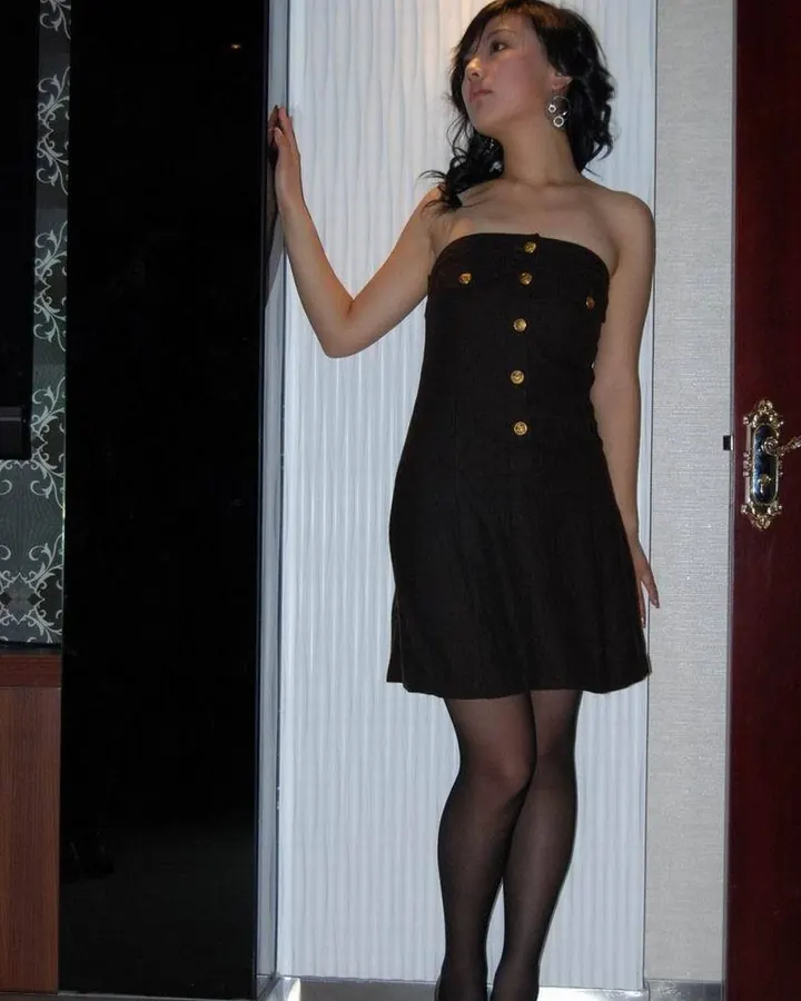 Femme asiatique en robe noire, debout près d'une porte, regardant l'appareil avec un léger sourire