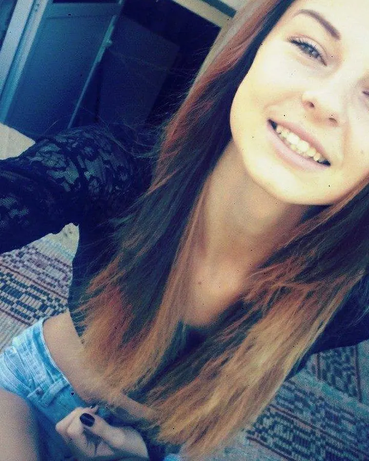 Femme en haut noir, cheveux longs bruns, souriant dans un miroir