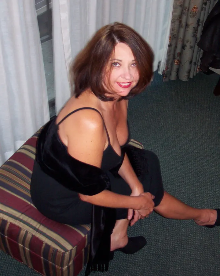 Femme en haut noir, cheveux bruns, souriant dans un salon
