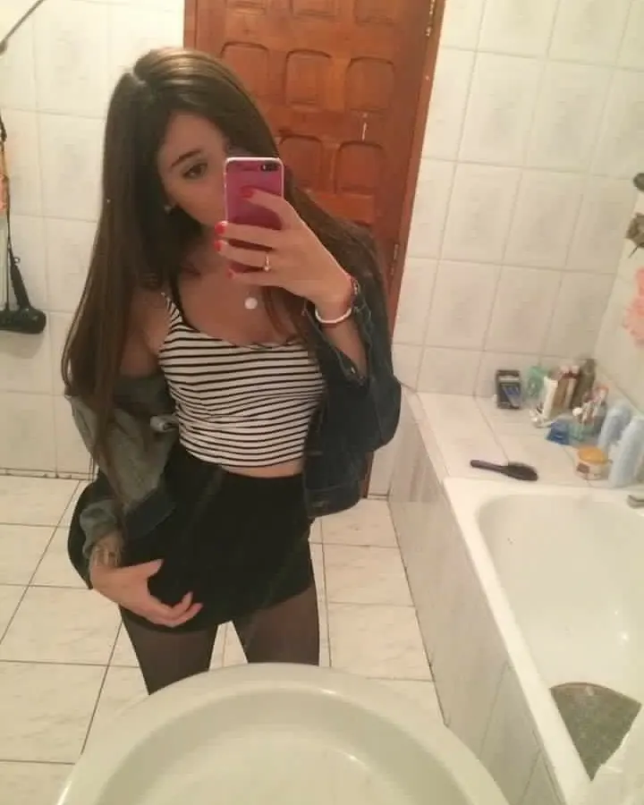 Femme en haut noir moulant, collants et talons, posant près d'une voiture bleue