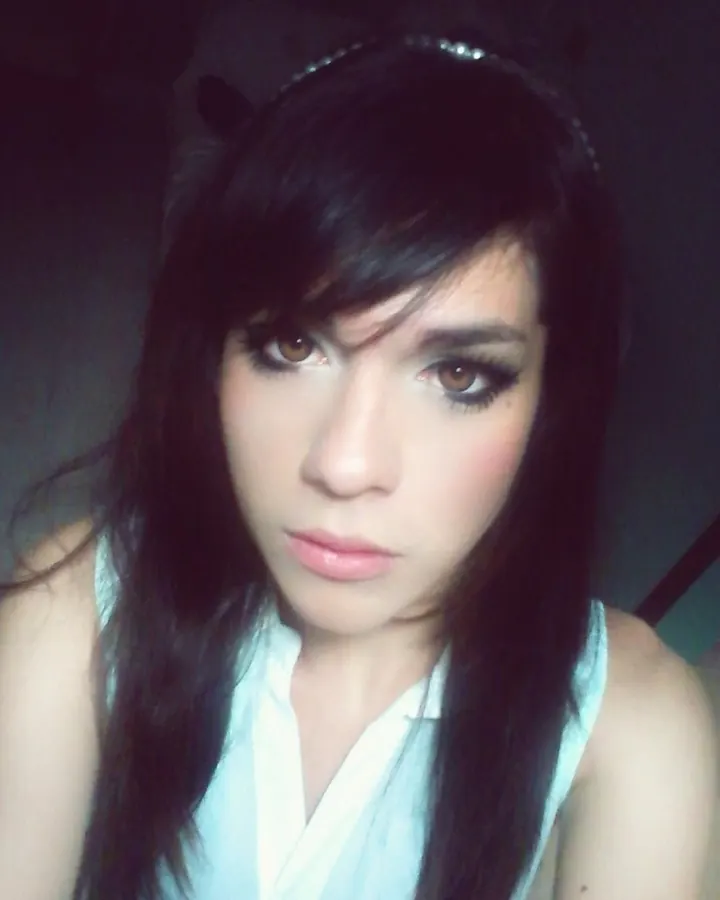 Femme aux cheveux noirs, regard intense, en chemise claire dans une pièce sombre