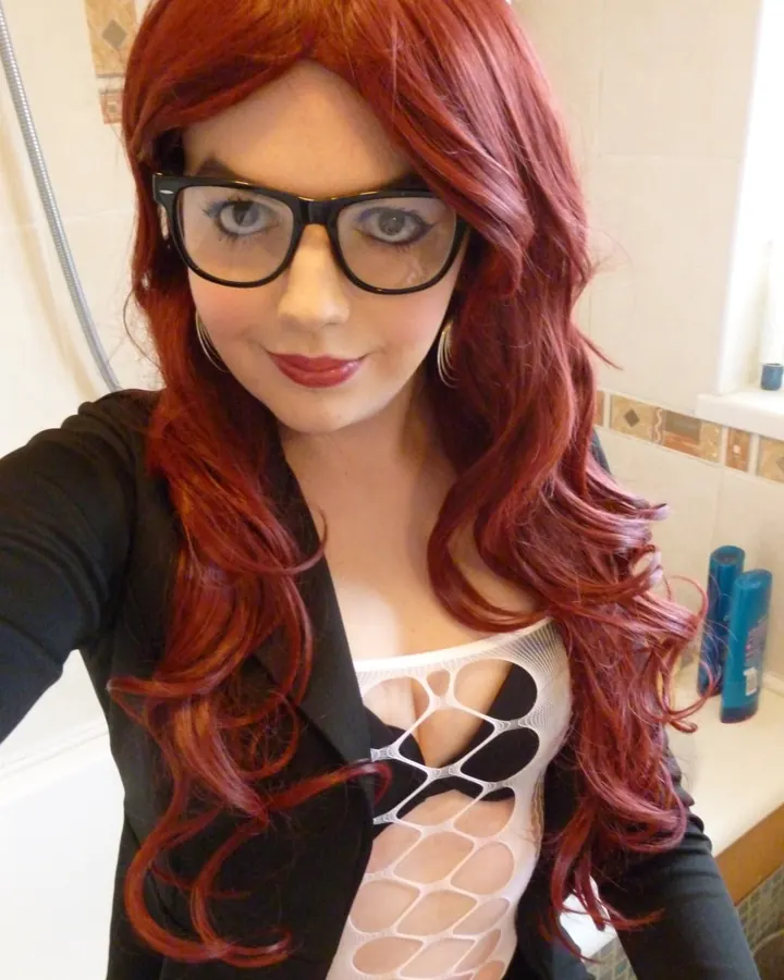 Femme aux cheveux roux, en robe noire avec dentelle, assise sur un canapé en cuir dans un salon
