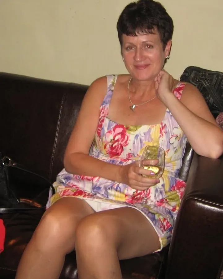 Nadia assise sur un canapé en robe fleurie avec un verre