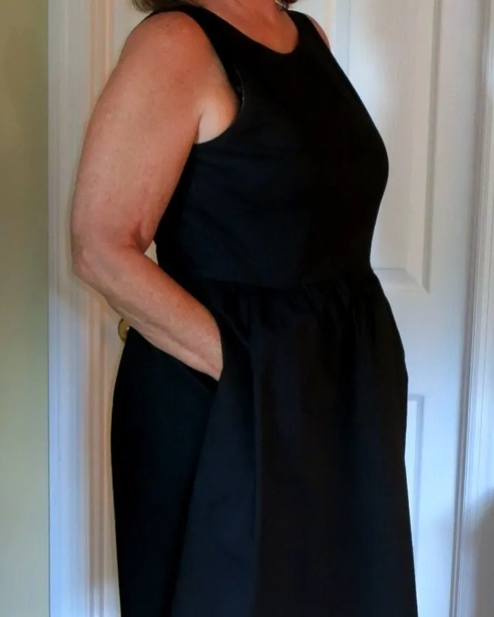 Inès debout en robe noire près d'une porte blanche