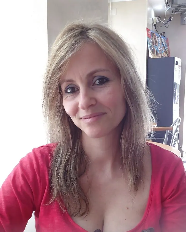 Femme mature aux cheveux gris, pull rouge, regard vers l’appareil.