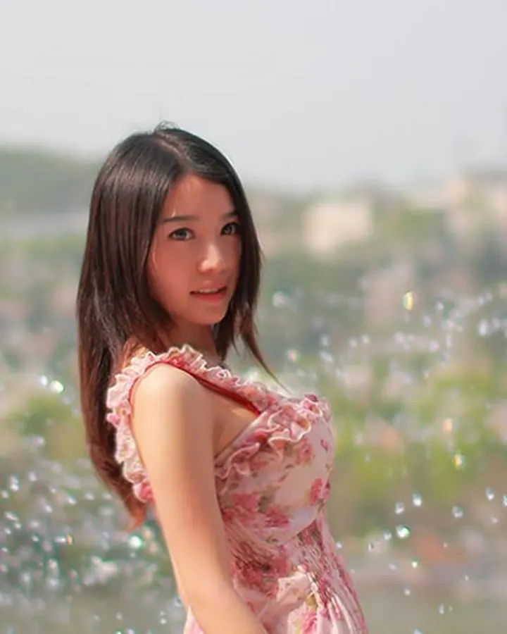 Jeune femme asiatique en robe fleurie rose, souriante, entourée de bulles de savon en extérieur
