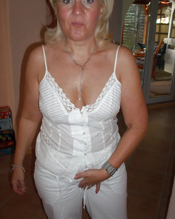 Femme européenne aux cheveux blonds platine, en tenue blanche, nue, debout près d’une piscine, regardant par-dessus son épaule