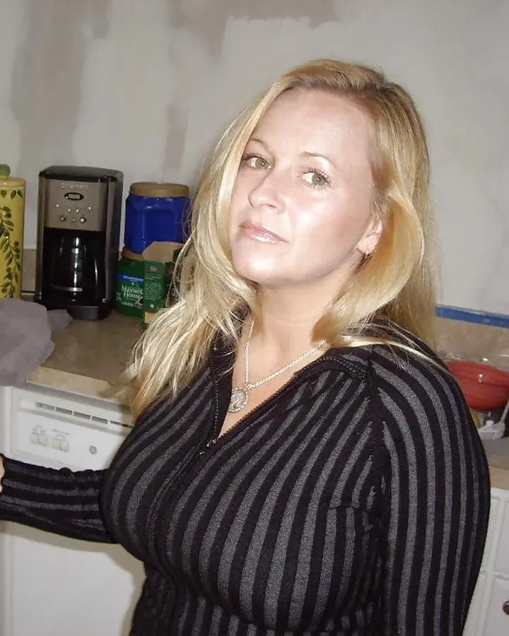 Femme blonde en pull rayé noir et gris, debout dans une cuisine, regardant vers l'appareil