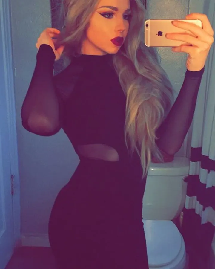 Femme blonde en robe noire transparente, assise près d'une fenêtre, regardant l'appareil