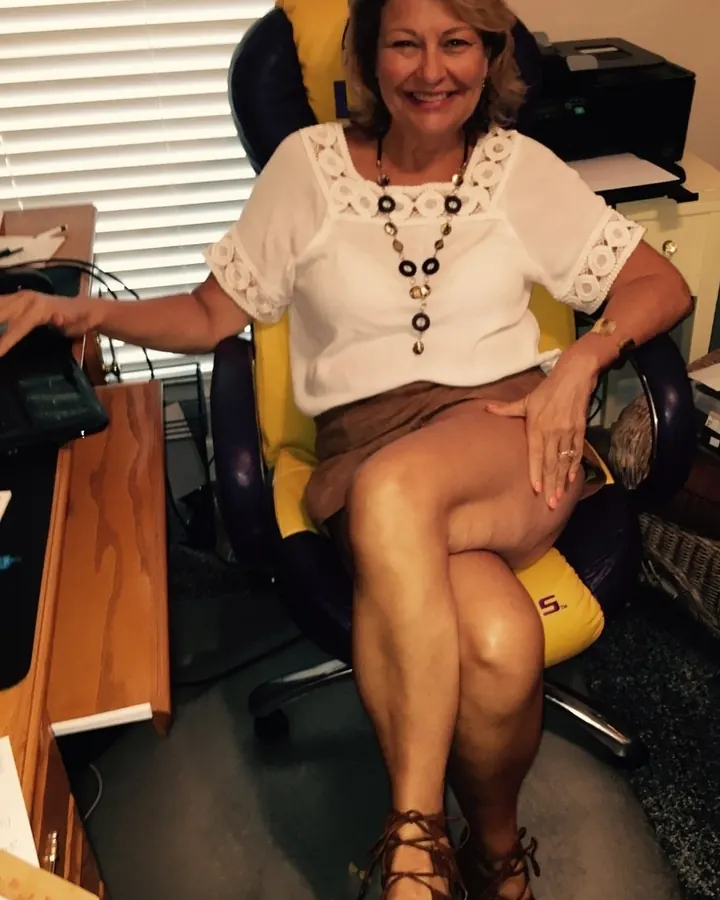 Femme assise sur un canapé, portant une robe rose vif, les jambes croisées, dans une pièce décorée avec goût.