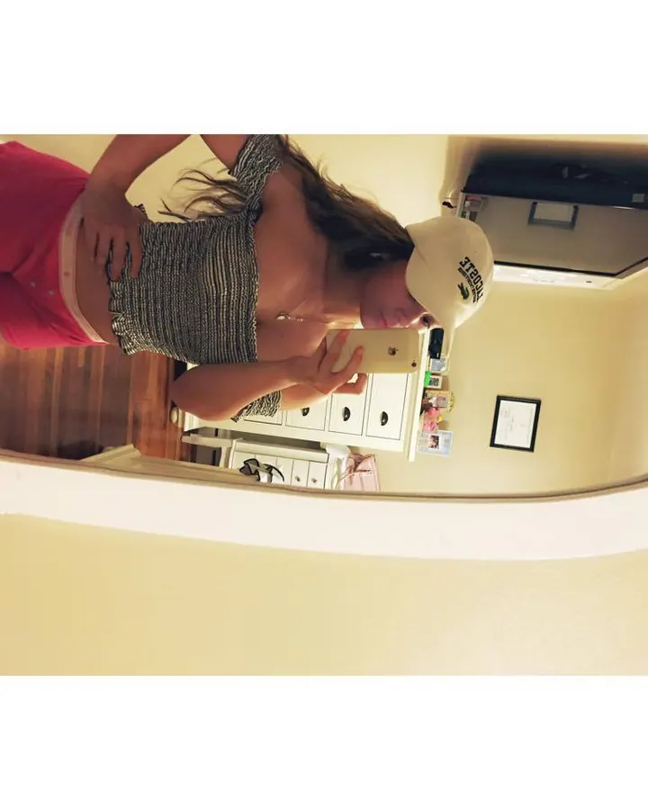 Femme en tenue décontractée (top rayé, short rose) prenant un selfie devant un miroir.
