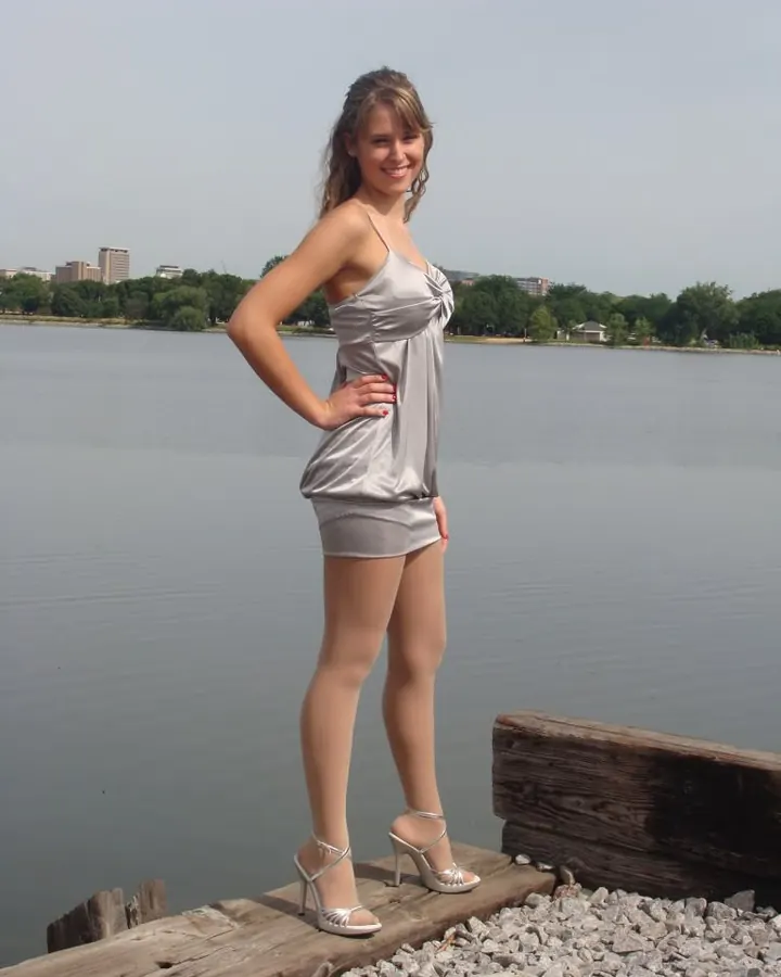 Femme aux cheveux bruns en haut blanc et jupe courte rayée, posant dehors.
