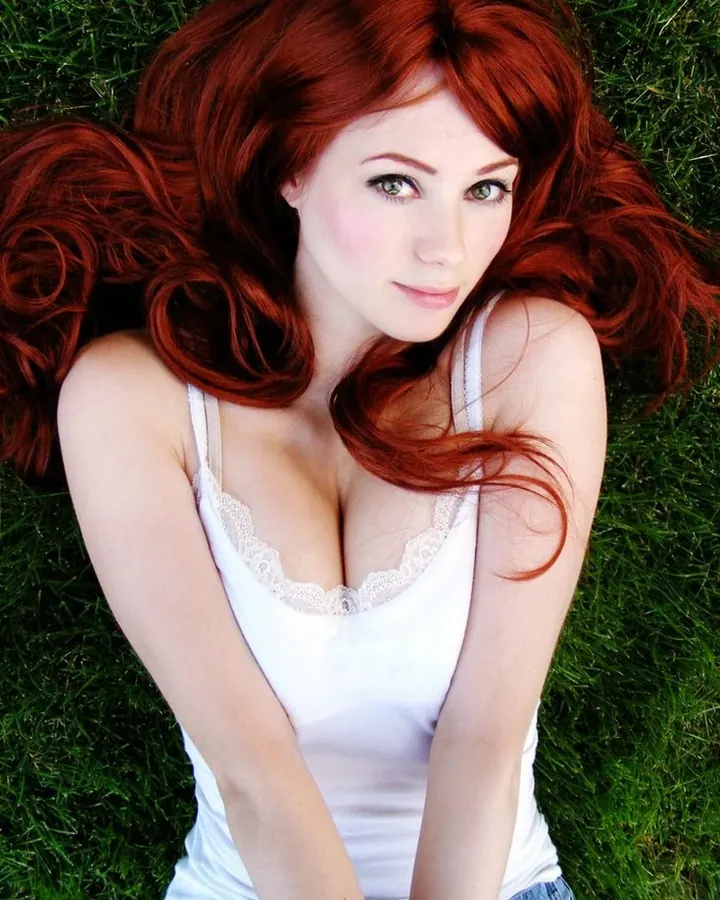Femme aux cheveux roux en haut blanc, posant dehors.