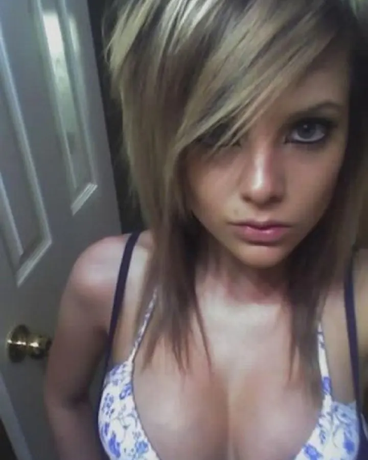 Jeune femme blonde aux yeux bleus en soutien-gorge à motifs bleus et blancs, regardant directement l'appareil devant une porte blanche.