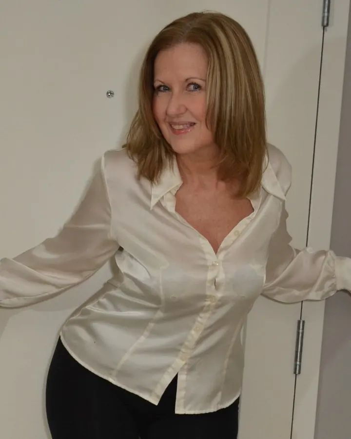 Femme blonde en robe noire, allongée sur un canapé, souriant à la caméra