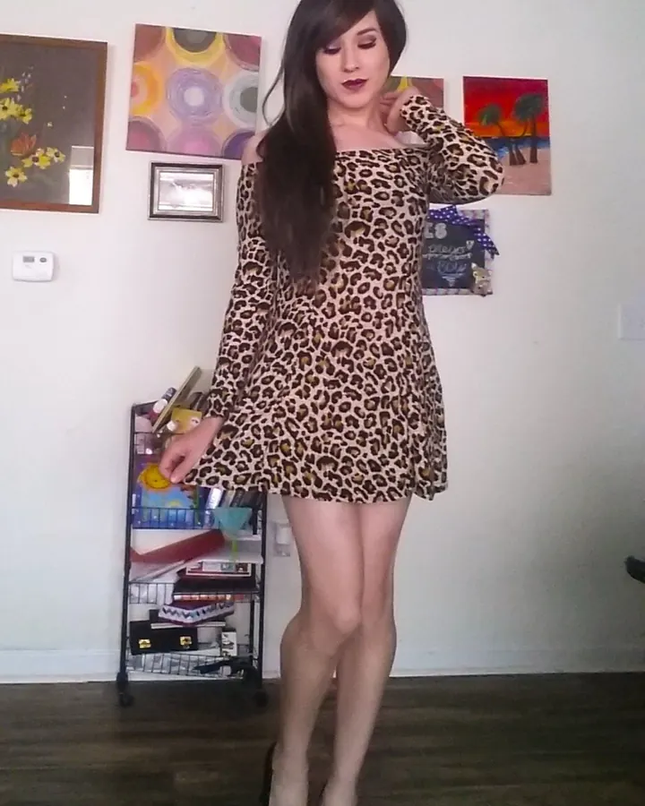 Femme en sous-vêtements noirs, posant sur un lit, vue de dos, dans une chambre aux murs roses
