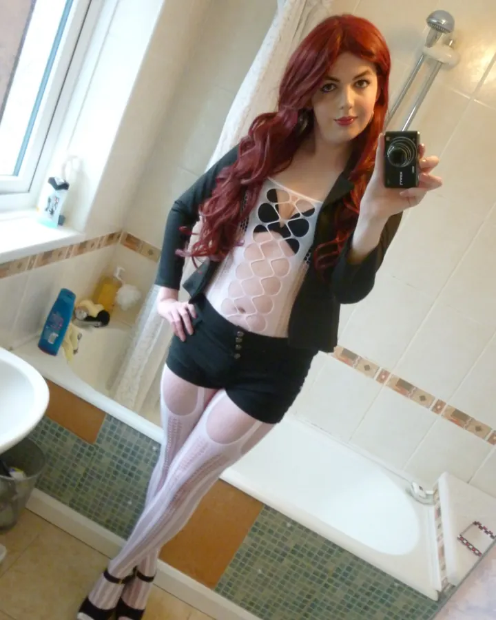 Femme en tenue noire, posant sur un lit, vue de dos, dans une chambre aux murs roses