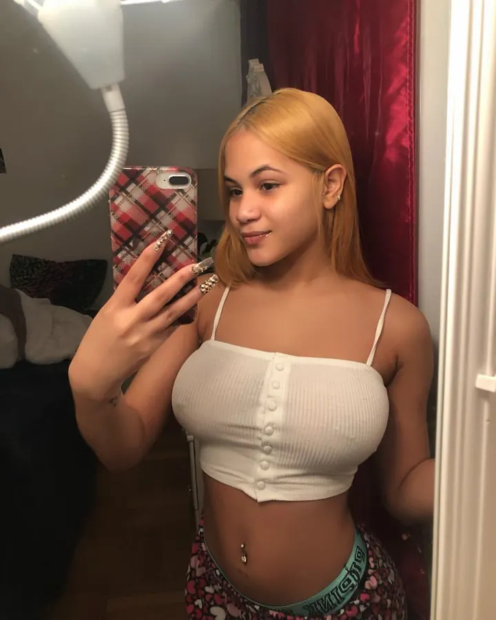 Femme en crop-top blanc, prenant un selfie dans un miroir, souriante, regardant l'appareil