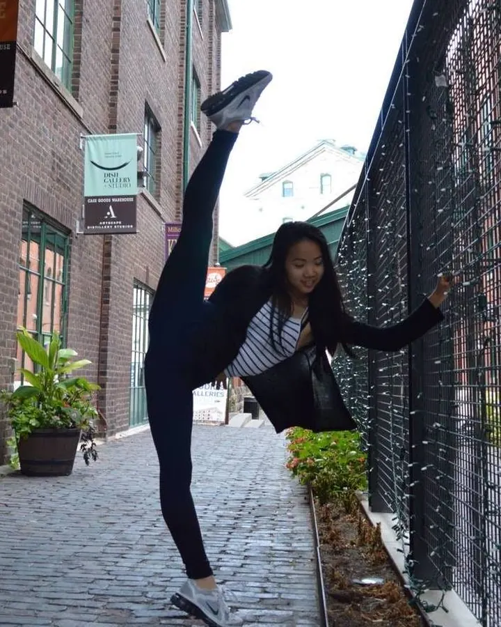 Femme en tenue de danse, faisant une extension sur un trottoir, souriante, regardant l'appareil