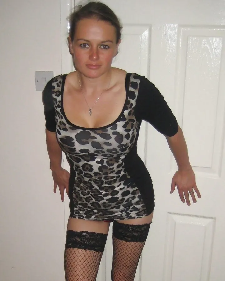 Femme en robe imprimée léopard, collants noirs, posant devant une porte blanche.
