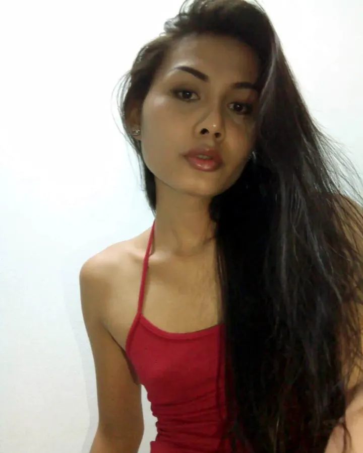 Femme brune regardant l'appareil photo, vêtue d’un haut rouge, avec les cheveux longs et lisses.