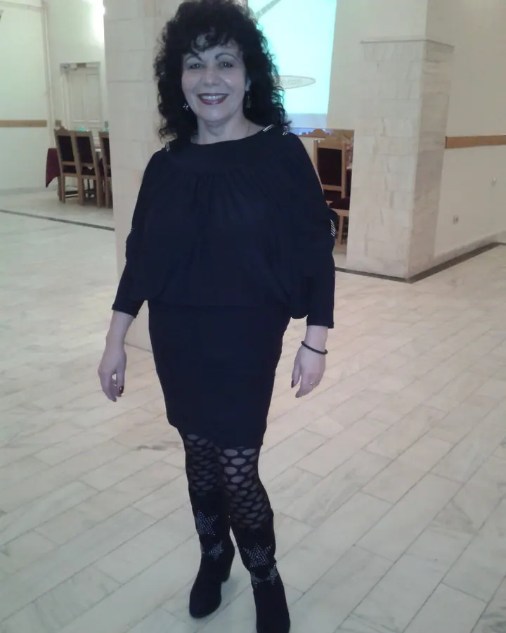 Femme aux cheveux noirs bouclés, souriante, en robe noire et collants à motifs, dans un hall avec sol en marbre