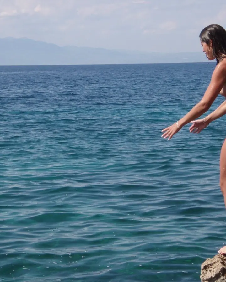 Femme nue, portant un haut transparent blanc, les bras croisés, regardant l'objectif.