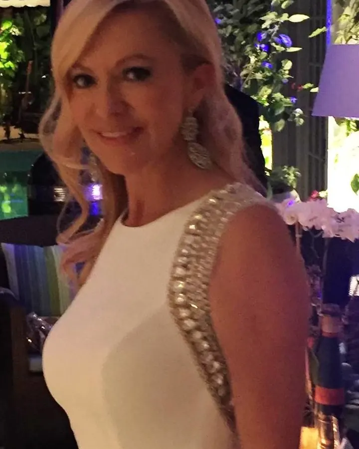 Femme blonde, yeux marrons, en haut blanc, regardant l'objectif avec assurance.