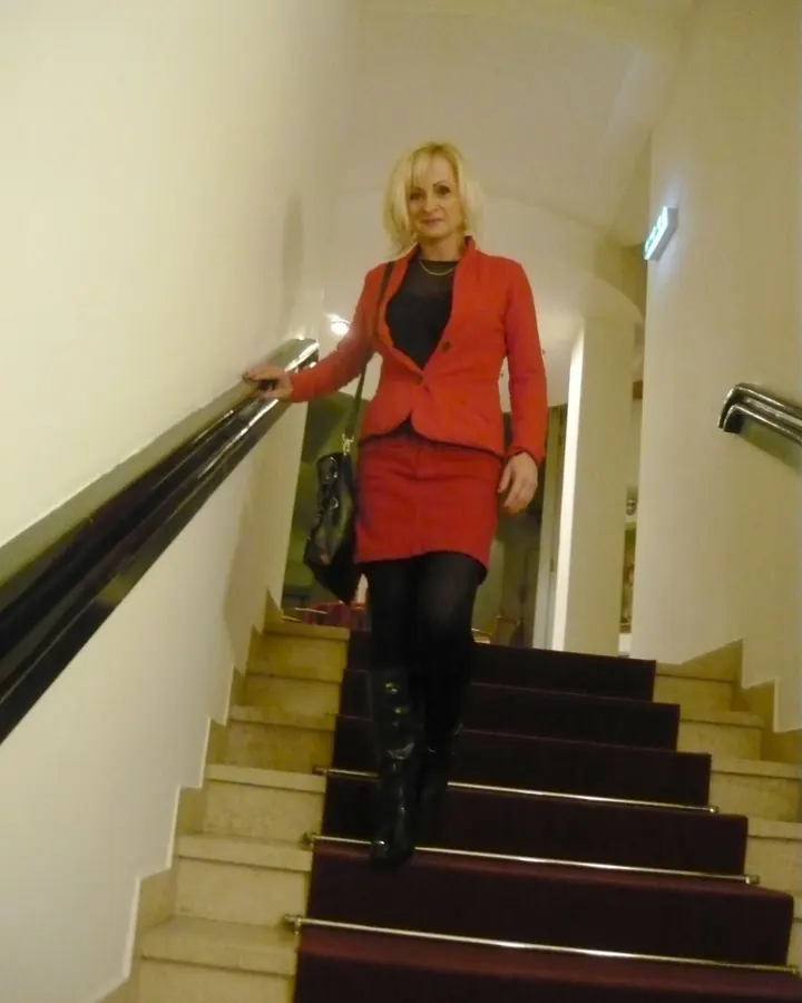 Femme blonde, yeux marrons, en chemise grise, assise à un bureau, regardant l'objectif.